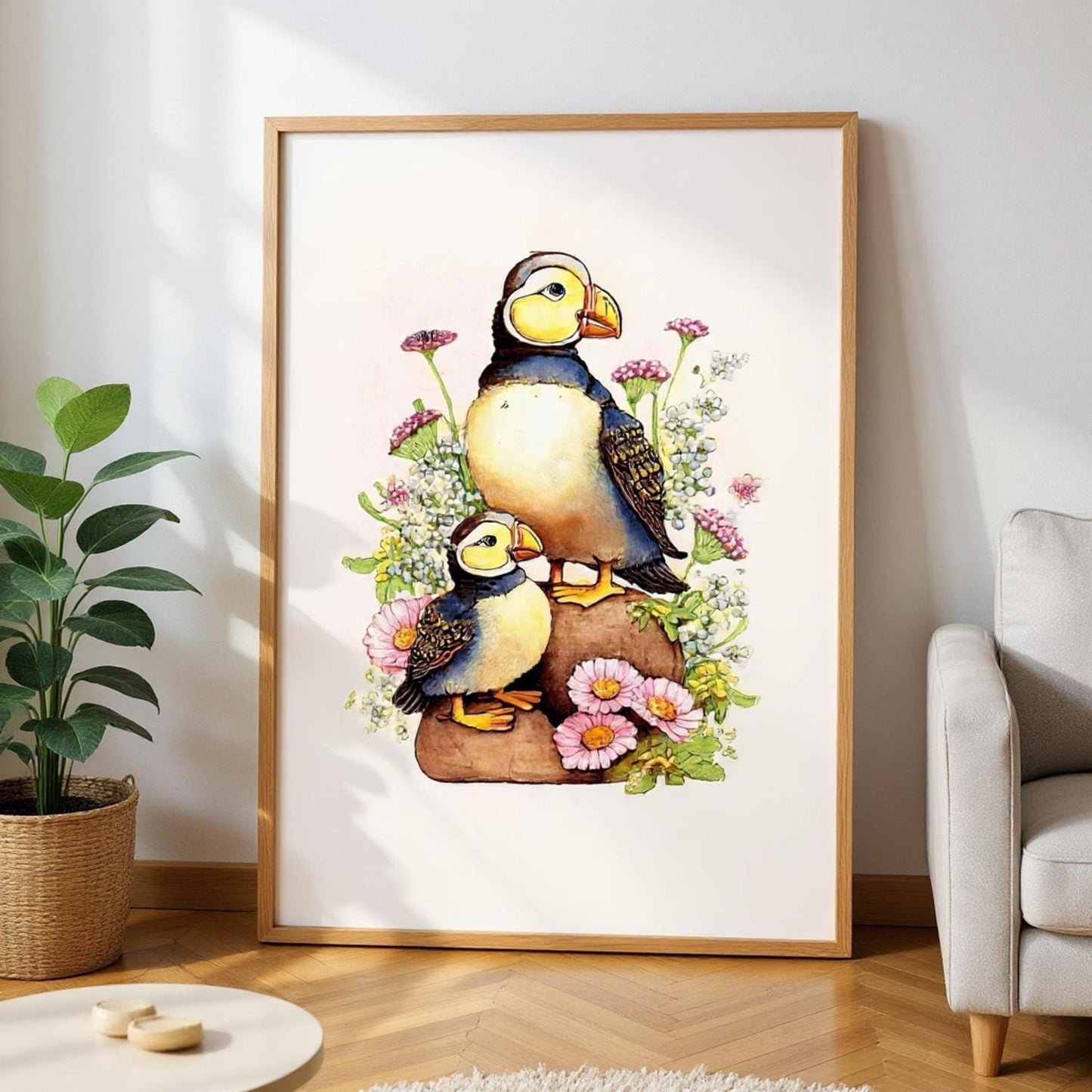 A framed painting depicting two puffins sitting on rocks surrounded by flowers and plants.