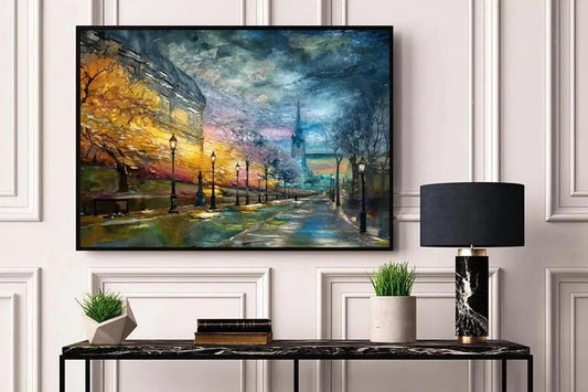 a large painting of a city street scene hanging on a wall, with a black table below it holding a lamp, a plant, and some books.